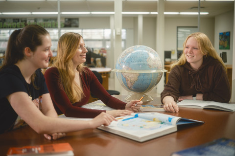 Trois étudiantes regardent un globe terrestre