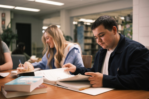 Un étudiant et une étudiante sont assis à une table regardant leur livre de cours