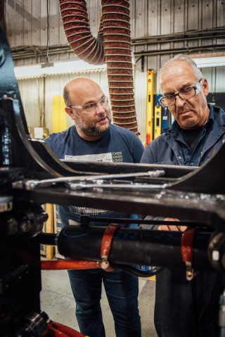 Joël et son collègue discute près d’une machine dans leur environnement de travail.